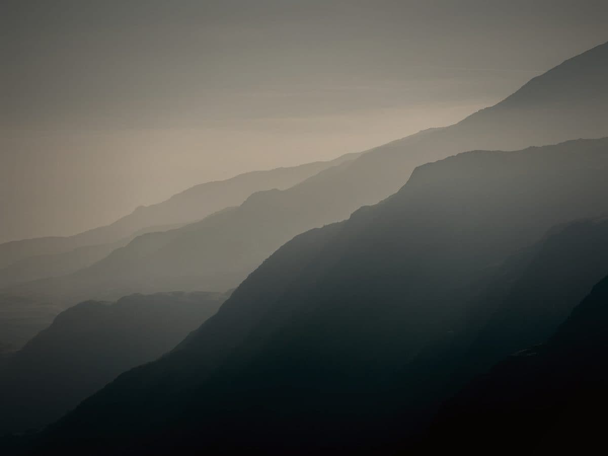 Layered ridgelines receding into morning mist, looking out across open land towards the horizon.